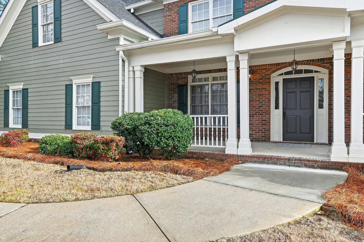 White home exterior with front entry porch, columns, and manicured landscaping